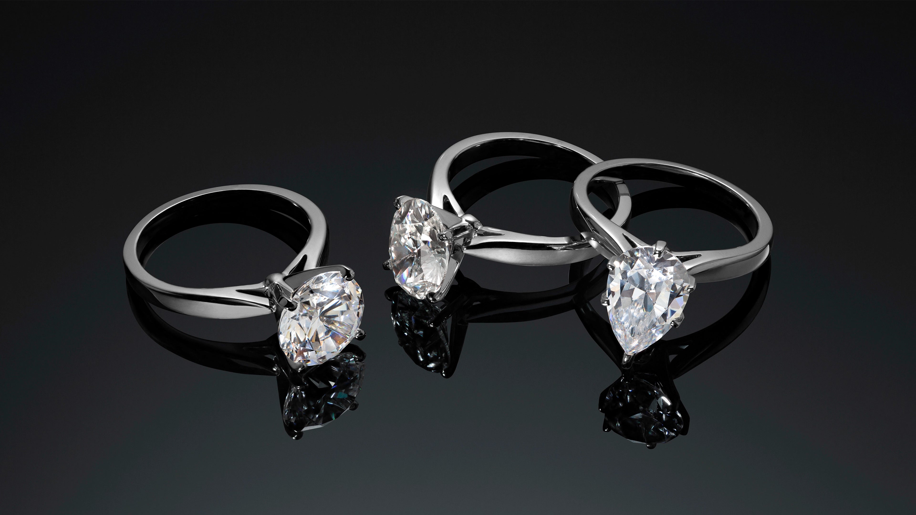 Three ALTR Created Diamond engagement rings; round, oval, and pear cut, in 14k white gold on a reflective black surface