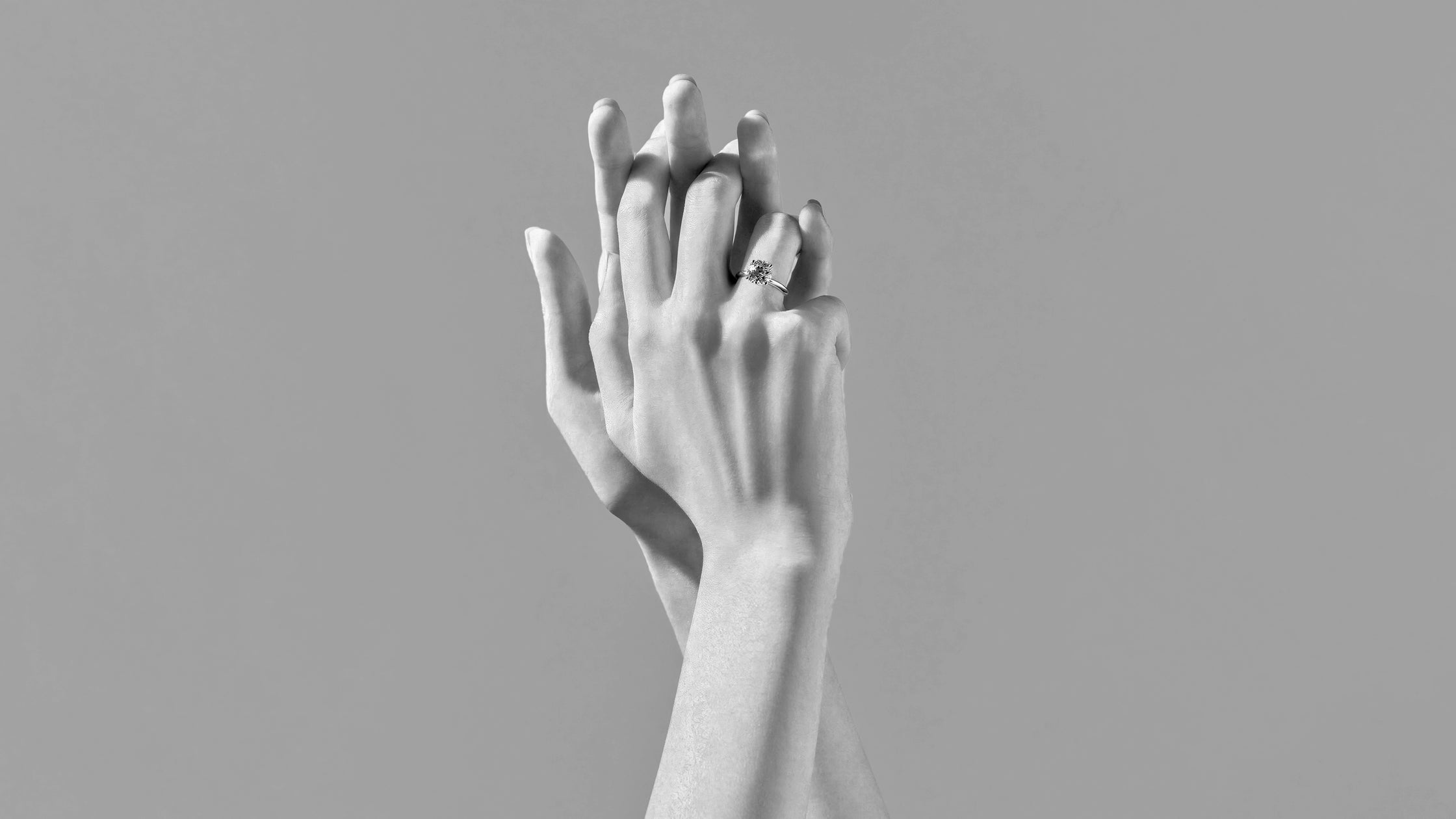 Black and white close-up of two hands intertwined, featuring a brilliant ALTR lab-grown diamond ring.