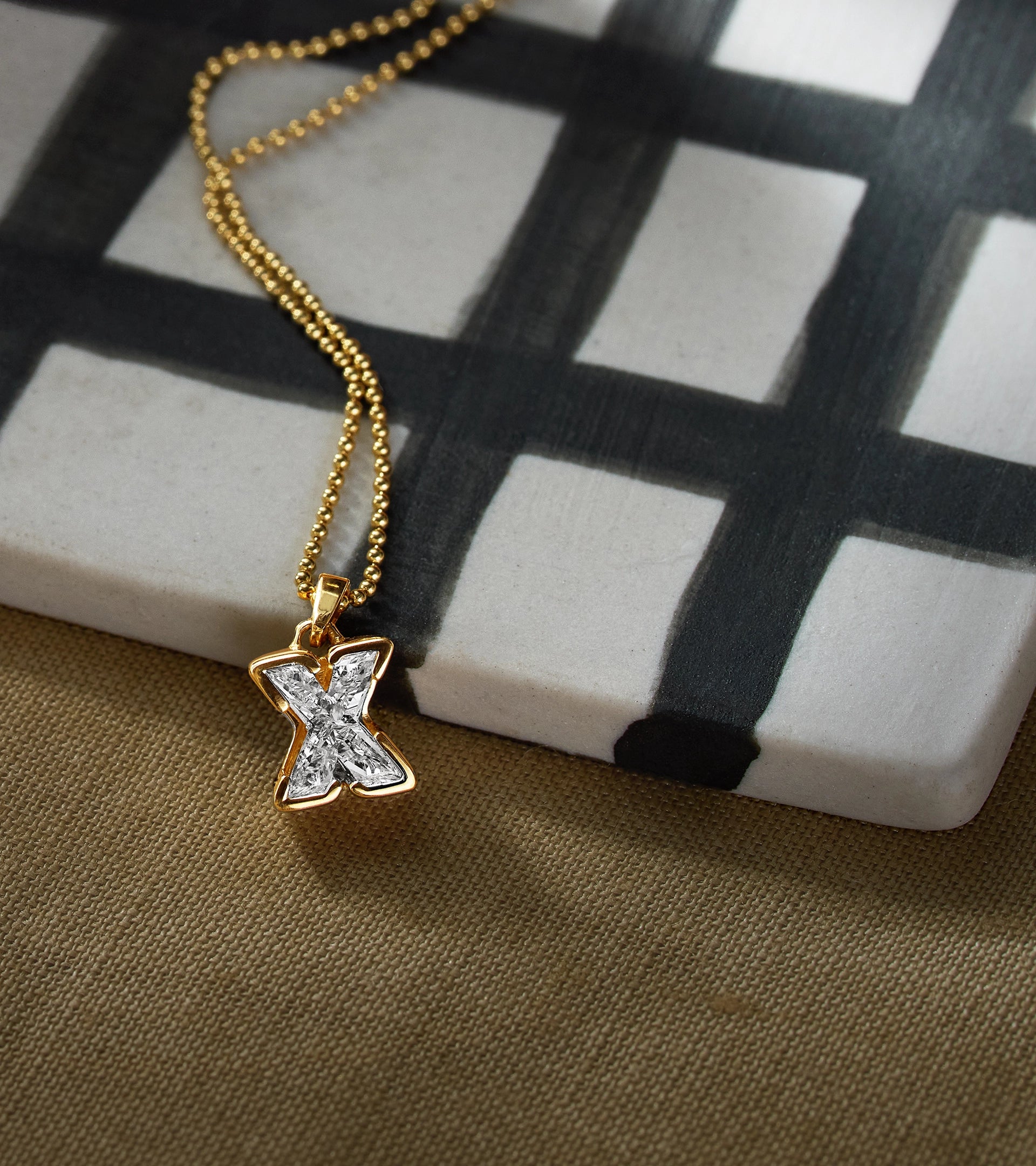 ALTR J'evar TYPE "X" initial solitaire diamond necklace pendant on a checkered surface.