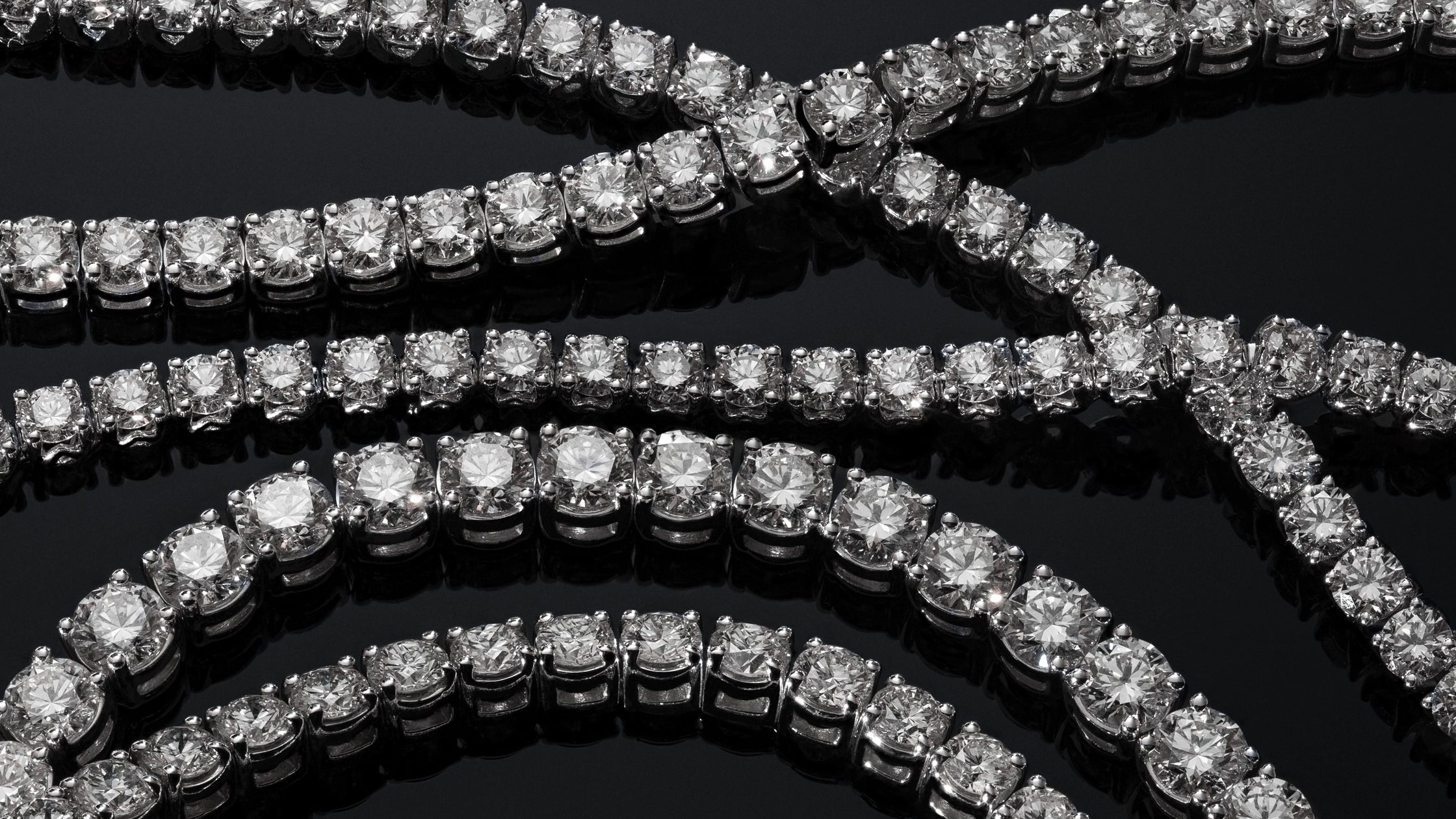 Rows of brilliant-cut ALTr created lab-grown diamond tennis bracelets displayed on a reflective black surface.