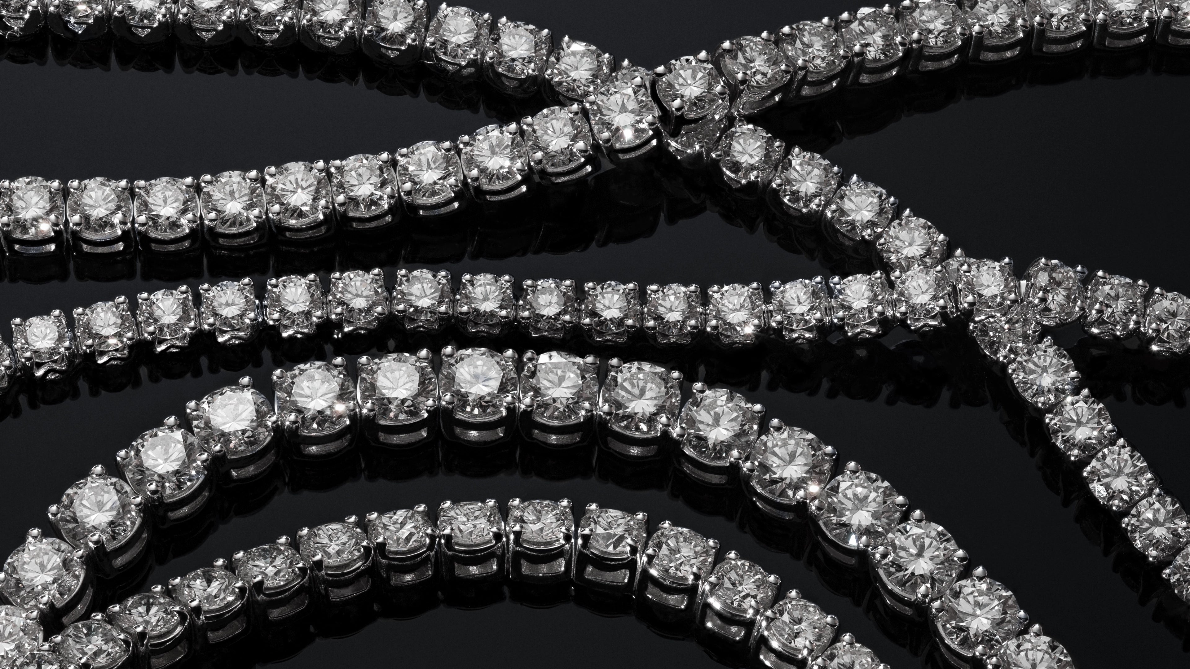 Rows of brilliant-cut ALTr created lab-grown diamond tennis bracelets displayed on a reflective black surface.