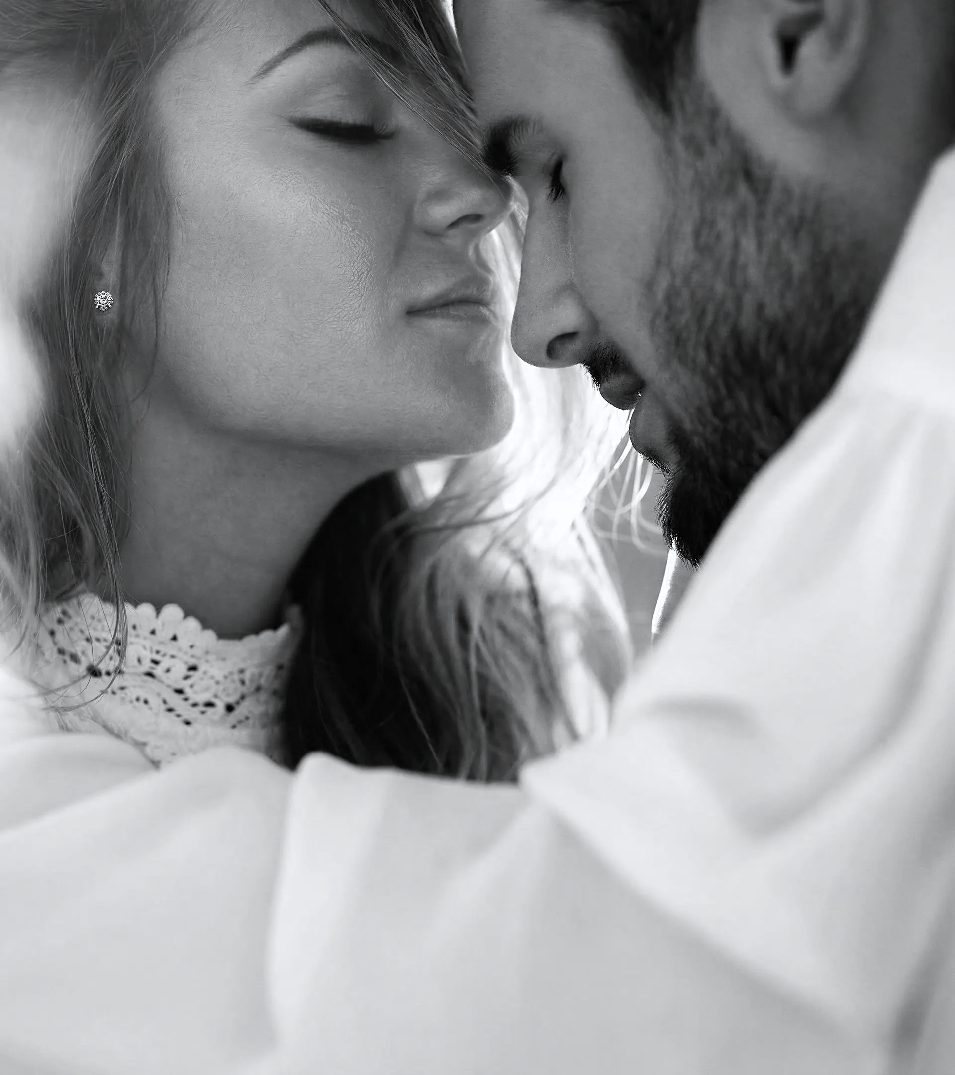 Black and white intimate portrait of a couple about to kiss, highlighting ALTR lab-grown diamond stud earrings worn by the woman.