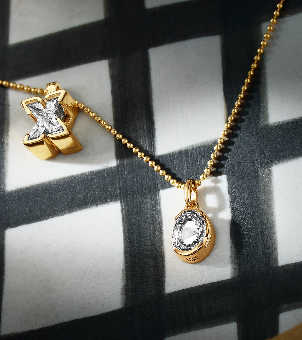 J'evar TYPE X and O solitaire initial letter pendant necklaces in 18k recycled gold on a checkered patterned surface.