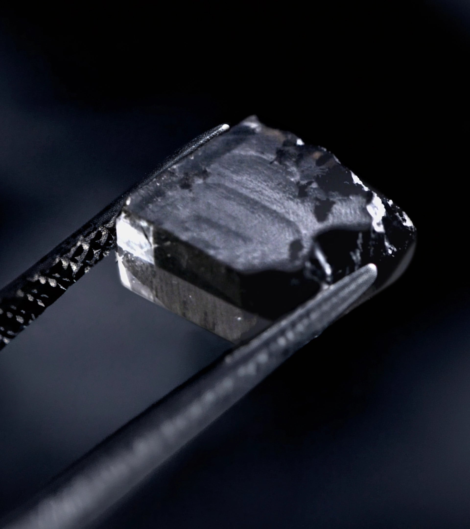 Tweezers holding a dark, uncut, rough lab-grown diamond during the ALTR's diamond manufacturing and inspection process.