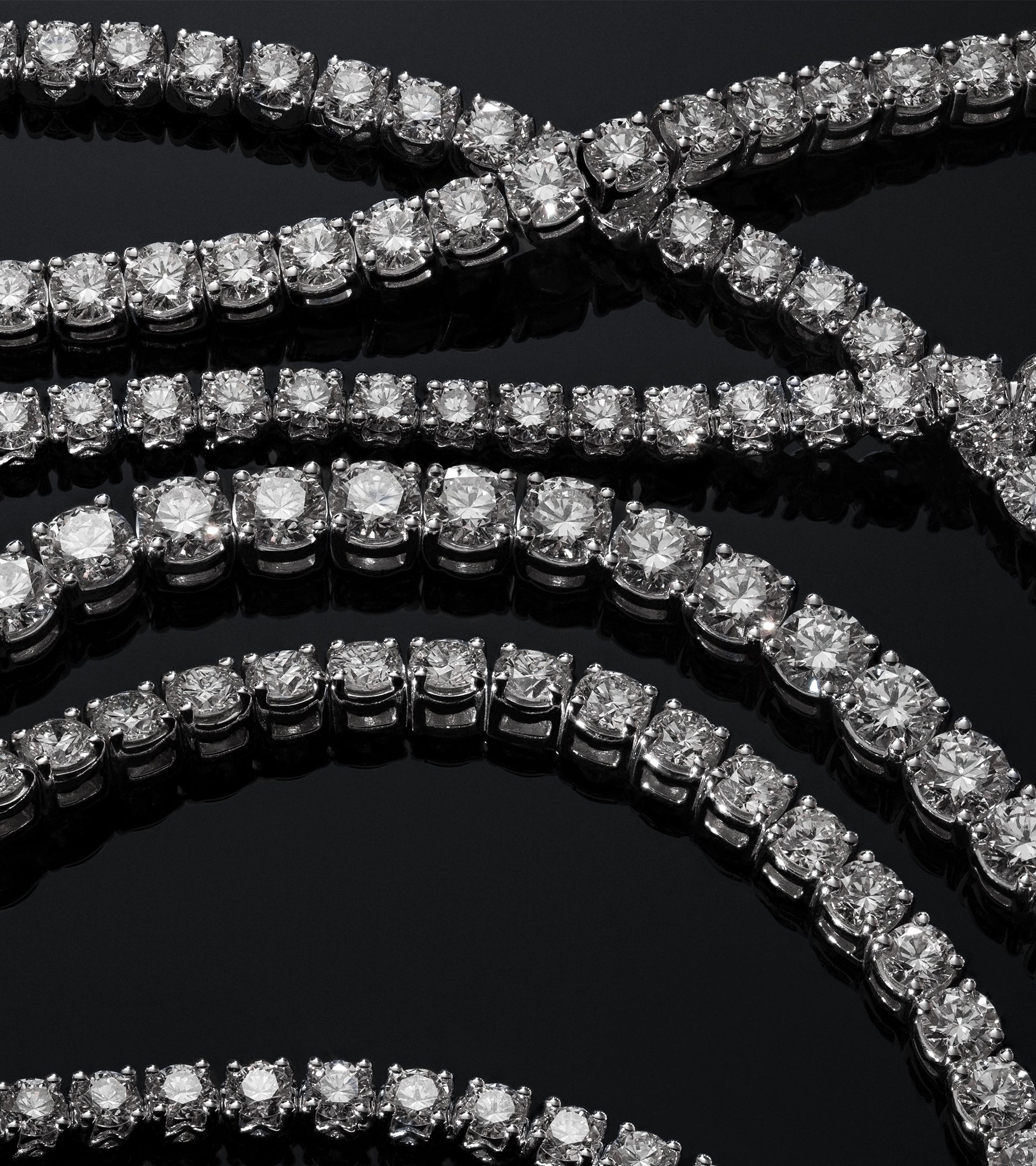 Rows of brilliant-cut ALTR created diamond tennis bracelets displayed on a reflective black surface.