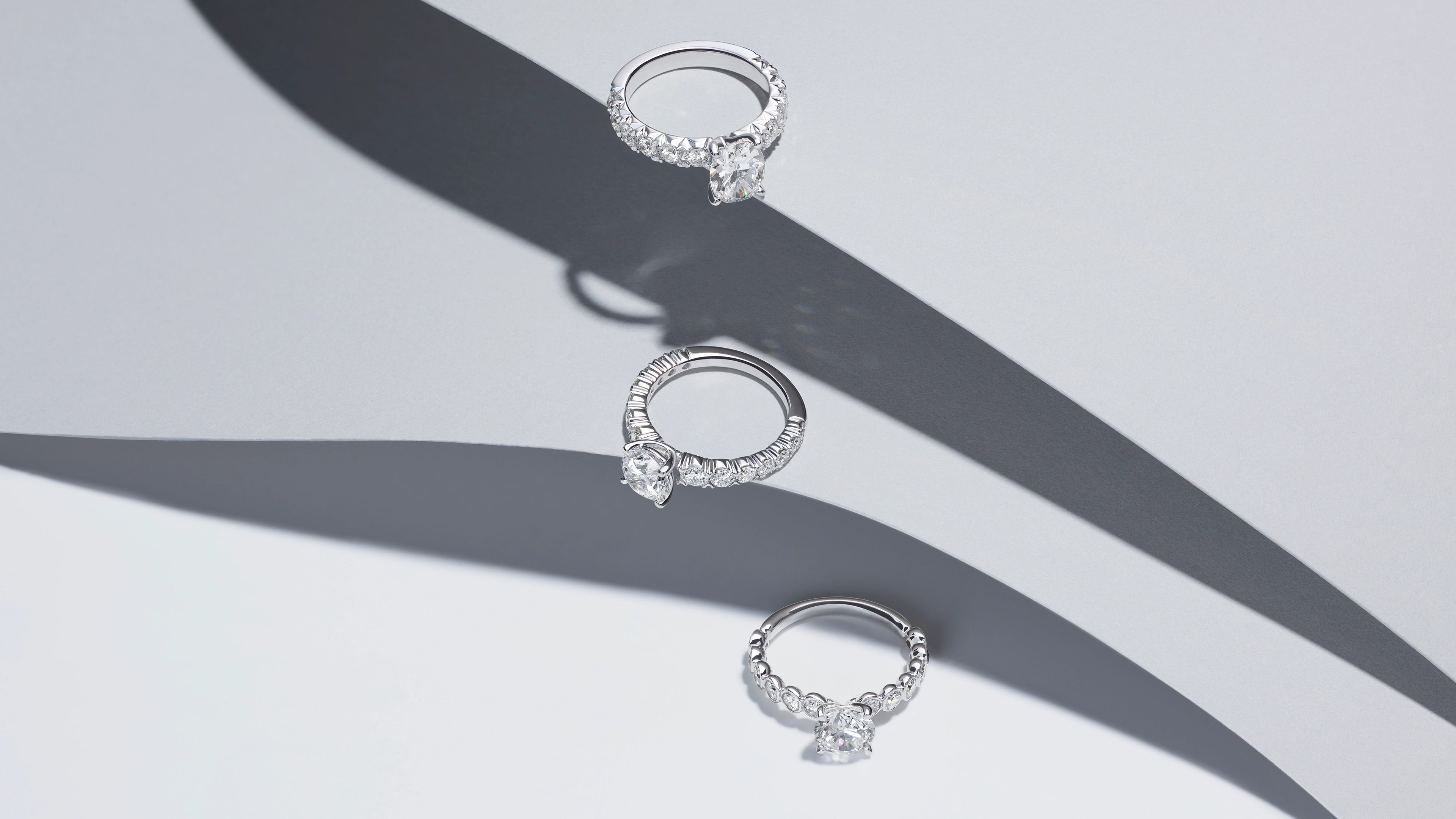 Three ALTR Created lab-grown diamond engagement rings in recycled white gold stacked vertically against a sleek white and grey architectural background.