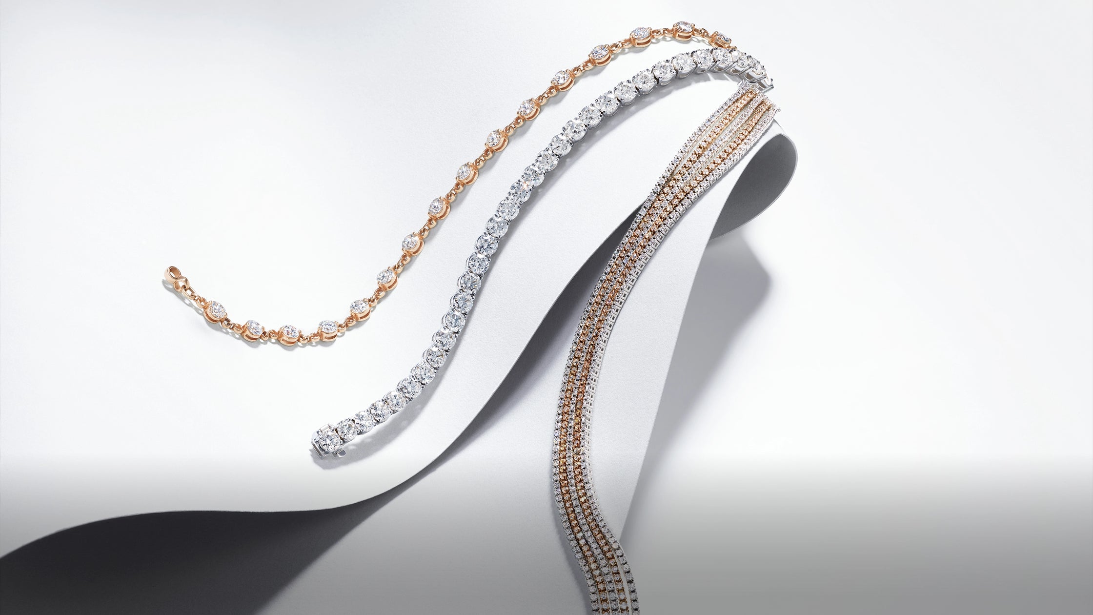 A curated collection of rose gold and white gold lab-grown diamond bracelets draped over a white display.