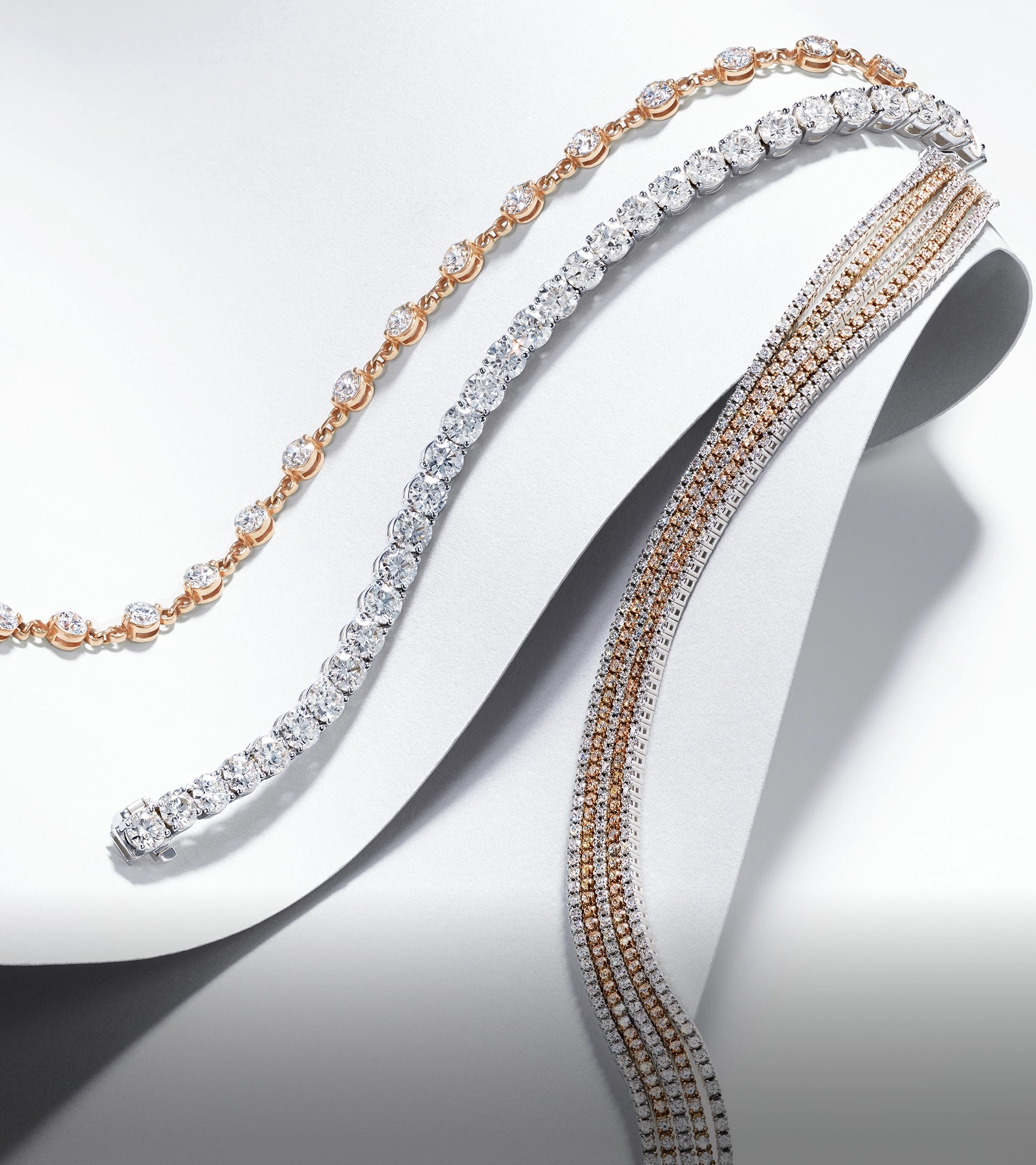 A curated collection of rose gold and white gold lab-grown diamond bracelets draped over a white display.