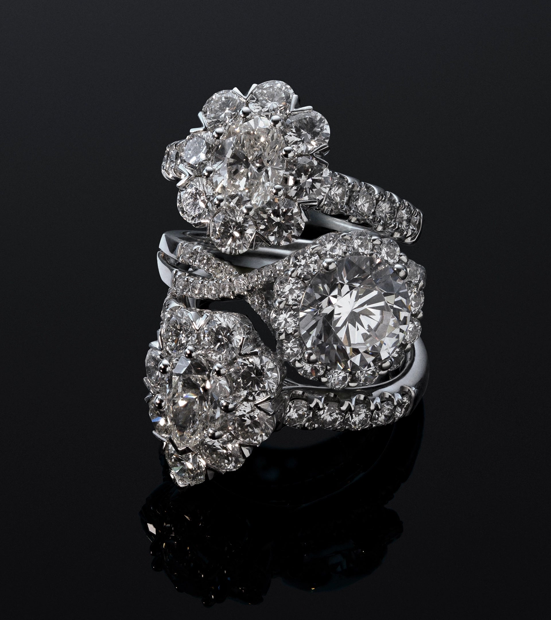 Stacked lab-grown diamond rings including halo and floral-inspired cluster designs on a dark background.
